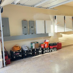 Organized garage interior featuring several electrical panels on the wall, with toolboxes and equipment neatly arranged along the floor.